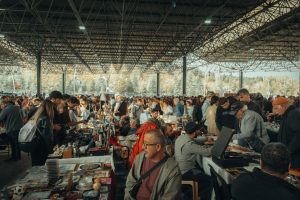 Bustling flea market with diverse crowd under a metal canopy, showcasing various goods. — Coronavirus disease 2019