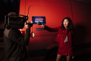 Asian female reporter with cameraman conducting a nighttime news broadcast beside a news van. — Sava Spin Casino: Il tuo play